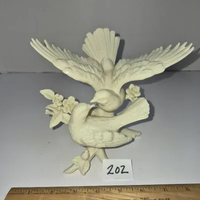 Sale Photo Thumbnail #343: Off-white resin or ceramic figurine depicting two birds perched on floral branches, featuring detailed outstretched wings.