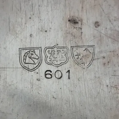 Sale Photo Thumbnail #900: Maker's mark and model number 601 stamped on a silver-plated or pewter surface.