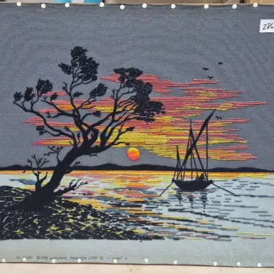Sale Photo Thumbnail #501: Vintage 1976 National Paragon Corp. embroidered crewel art piece depicting a sailboat at sunset near a silhouette tree, mounted on a board measuring approximately 28x22 inches.