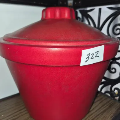 Sale Photo Thumbnail #560: Red ceramic covered casserole dish with a ribbed knob lid, shown resting on a shelf.