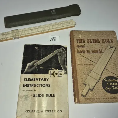 Sale Photo Thumbnail #311: Vintage Keuffel & Esser Co. slide rule with matching green protective sleeve, accompanied by two instructional manuals on operating slide rules.