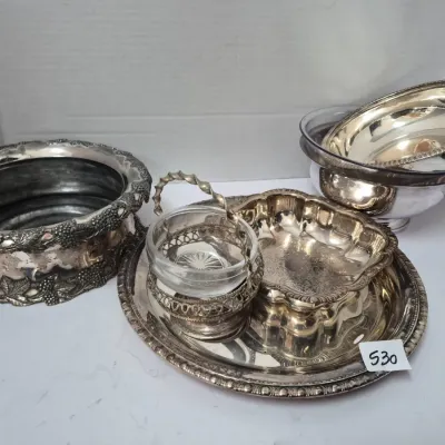 Sale Photo Thumbnail #916: Collection of silver-plated serving pieces, including bowls, trays, and a small glass condiment dish with a silver handle.