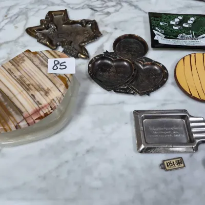 Sale Photo Thumbnail #136: Collection of vintage trinket dishes and small metal collectibles, including a Texas-shaped brass tray, a polished stone covered box, souvenir trays, and a Barton Distilling Co. dish.