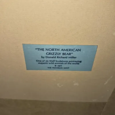 Sale Photo Thumbnail #599: Title label for 'The North American Grizzly Bear' wall sculpture by Donald Richard Miller for The Franklin Mint, 1977.