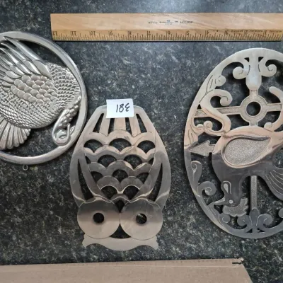 Sale Photo Thumbnail #661: Set of three vintage metal trivets, including a turkey, an owl, and a rooster design, shown with a 12-inch ruler for scale.