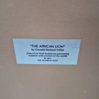 Sale Photo Thumbnail #596: Descriptive plaque for 'The African Lion' wall sculpture by Donald Richard Miller for The Franklin Mint, copyright 1977.