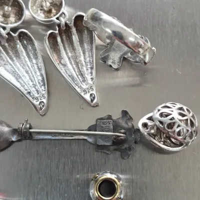 Sale Photo Thumbnail #849: Selection of sterling silver jewelry items, including a pair of dangle post earrings stamped 925, a brooch marked STERLING, a ring, and a charm.