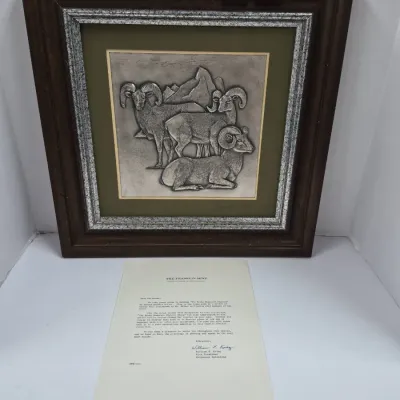 Sale Photo Thumbnail #600: Framed Franklin Mint sterling silver bas-relief plaque featuring bighorn sheep in a mountain landscape, complete with accompanying documentation letter. The relief artwork is double-matted in a dark wood frame measuring 18x18 inches.