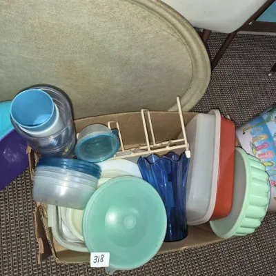 Sale Photo Thumbnail #556: Cardboard box filled with assorted vintage household items, including plastic Tupperware containers, a blue glass vase, a wire rack, and plastic bowls.