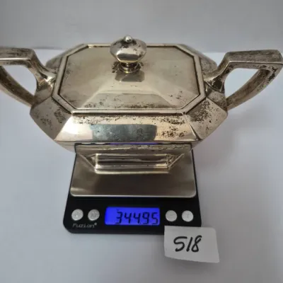 Sale Photo Thumbnail #892: Art Deco style silver-plated double-handled covered sugar bowl resting on a digital scale displaying 344.95 grams, showing heavy tarnish and patina.