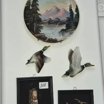 Sale Photo Thumbnail #543: Vertical wall arrangement featuring decorative plates, flying duck figurines, framed copper art, and a round ceramic heraldic shield plaque.