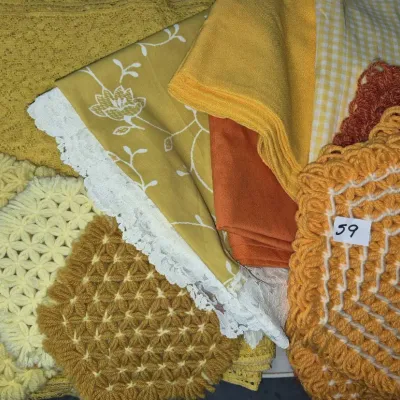 Sale Photo Thumbnail #92: Collection of vintage yellow and orange linens, including crocheted pot holders, a floral patterned napkin with lace trim, gingham fabric, and solid textiles.