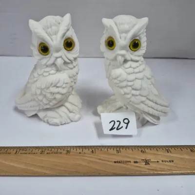Sale Photo Thumbnail #393: Pair of vintage white composite or resin owl figurines featuring prominent amber glass eyes, measuring approximately four inches tall.