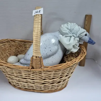 Sale Photo Thumbnail #284: Vintage ceramic duck figurine with speckled grey glaze and a fabric bonnet, resting in a woven wicker basket alongside artificial eggs.