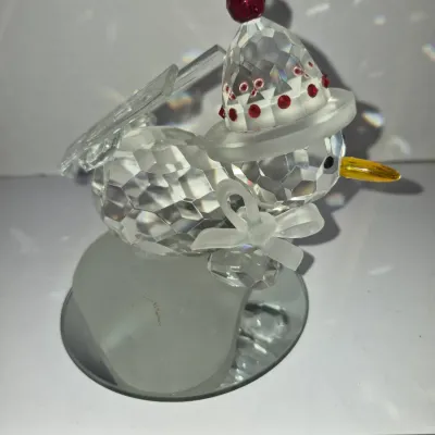 Sale Photo Thumbnail #415: Swarovski crystal snowman figurine featuring a hat with red rhinestone accents, yellow beak, frosted bow, and a reflective base.