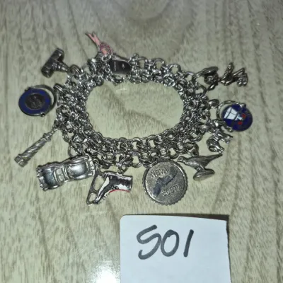 Sale Photo Thumbnail #863: Vintage sterling silver double-link charm bracelet featuring various travel and themed charms, including a Nova Scotia coin, vintage car, ice skate, lighthouse, and enamelled pieces.