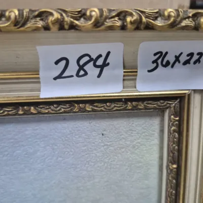 Sale Photo Thumbnail #496: Detail of an ornate gilt and off-white picture frame, marked lot 284 and measuring 36x22 inches.