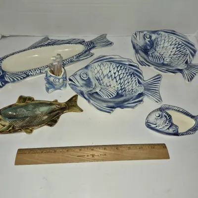 Sale Photo Thumbnail #774: Collection of ceramic fish-shaped serving dishes, toothpick holders, and trays in blue and white and natural glazed finishes, displayed with a wooden ruler for scale.