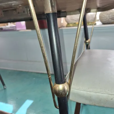 Sale Photo Thumbnail #842: Underside detail of a mid-century modern dining table leg with a black pole, brass hairpin accents, and a brass ball collar.