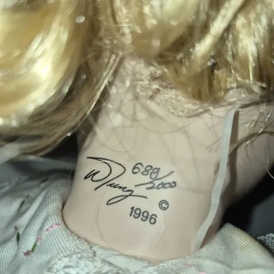 Sale Photo Thumbnail #211: Close-up of a porcelain doll's neck showing a maker's mark signature, copyright date of 1996, and hand-numbered edition 689/2000.