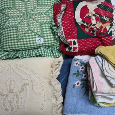 Sale Photo Thumbnail #198: Collection of vintage decorative pillows and household linens, including embroidered ruffled cushions, a Christmas-themed pillow, and stacked hand towels.