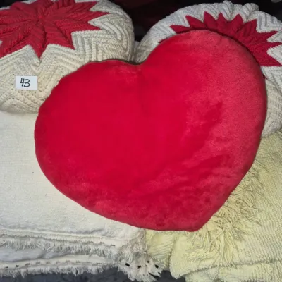 Sale Photo Thumbnail #68: Collection of decorative throw pillows and blankets, including a red plush heart pillow, star-patterned round knit cushions, and fringed textiles.