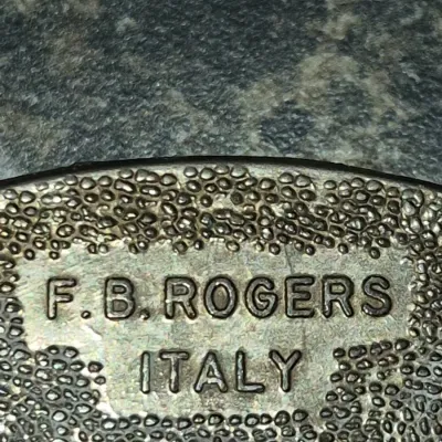 Sale Photo Thumbnail #664: Maker's mark closeup for F.B. Rogers, stamped 'F.B. ROGERS ITALY' on a textured metal surface.