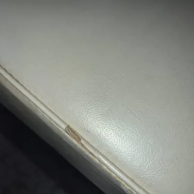 Sale Photo Thumbnail #10: Close-up view of off-white vinyl upholstery showing a small tear and wear along the piped edge.