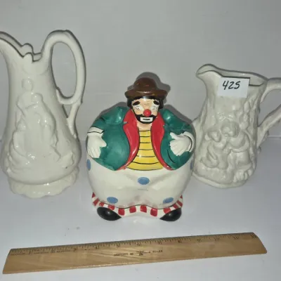 Sale Photo Thumbnail #742: Vintage ceramic clown cookie jar flanked by two white embossed pottery pitchers.