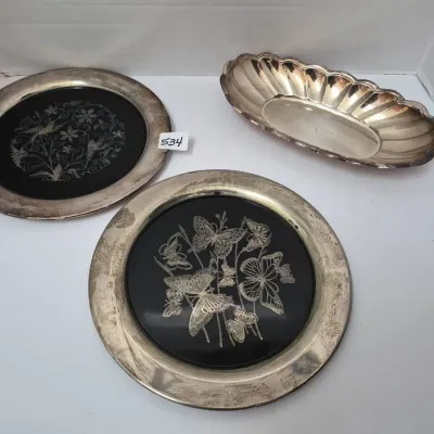 Sale Photo Thumbnail #922: Set of three vintage silver-plated items, including two decorative round trays with black centers featuring etched floral and butterfly designs, alongside a scalloped oval dish.
