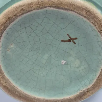 Sale Photo Thumbnail #261: Underside of a celadon green crackle-glaze ceramic vessel showing a unglazed foot ring and maker's mark.