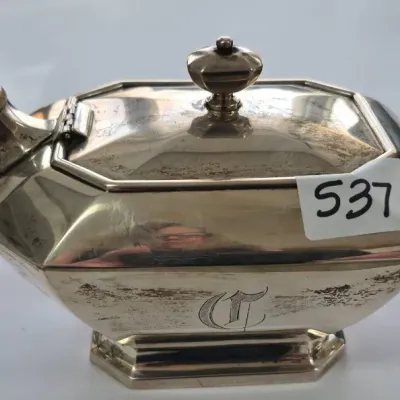 Sale Photo Thumbnail #928: Antique octagonal silver teapot featuring an engraved monogram and an angular handle, showing light surface tarnish.
