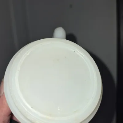 Sale Photo Thumbnail #571: Underside of a vintage white milk glass mug, showing a smooth unmarked base and side handle.
