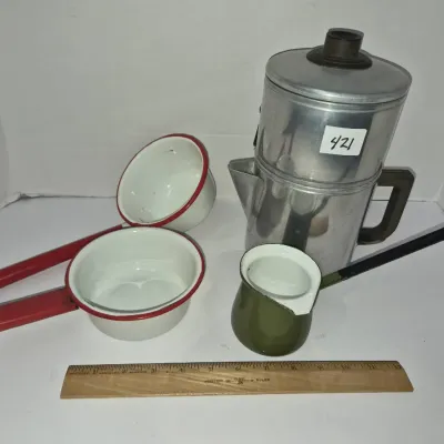 Sale Photo Thumbnail #736: Vintage aluminum camping percolator pot alongside a assortment of enamelware pans and a small green creamer vessel, displayed with a wooden ruler for scale.