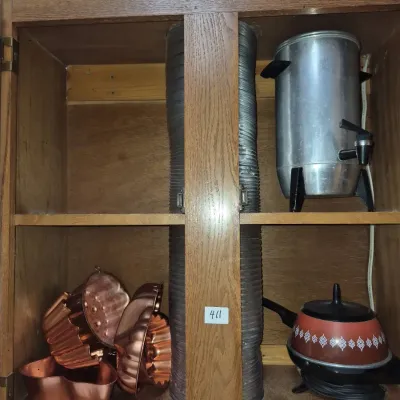 Sale Photo Thumbnail #724: Wooden wall cabinet storing vintage copper-colored gelatin and cake molds, a large aluminum coffee urn, and a vintage patterned hot pot.