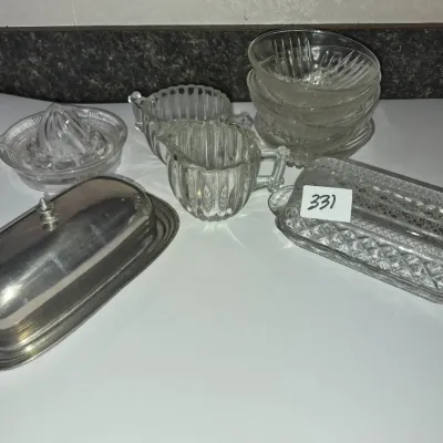 Sale Photo Thumbnail #577: Collection of vintage table accessories including a silver-tone covered butter dish, cut glass butter dish, ribbed cream and sugar set, glass juicer, and stacked glass bowls.