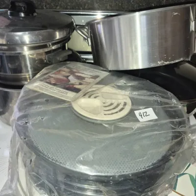 Sale Photo Thumbnail #725: Collection of kitchenware including stainless steel stock pots, an electric food dehydrator in plastic packaging with manual, and non-stick cookware.