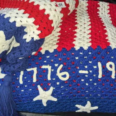 Sale Photo Thumbnail #87: Handmade crochet American Bicentennial blanket featuring red, white, and blue patriotic stars and stripes motifs with "1776-1976" lettering and fringe tassels.