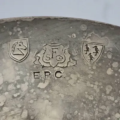 Sale Photo Thumbnail #918: Close-up detail of maker's marks on a tarnished silver-plated item, featuring 'E.P.C.', a knight logo, and Sheffield Silver Co. crest.