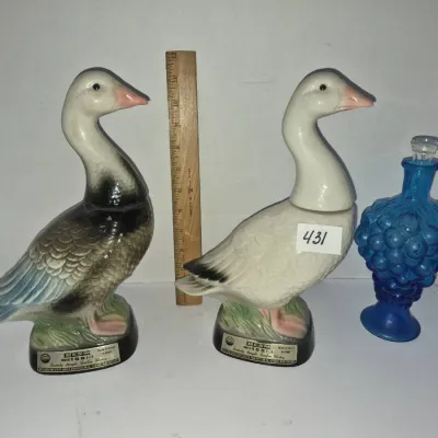 Sale Photo Thumbnail #749: Two vintage Jim Beam ceramic duck-shaped bourbon decanters paired with a blue pressed glass grape-motif bottle with stopper.