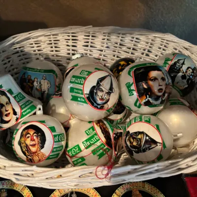 Collection of vintage Wizard of Oz glass ball and bell ornaments displayed inside a white wicker basket.