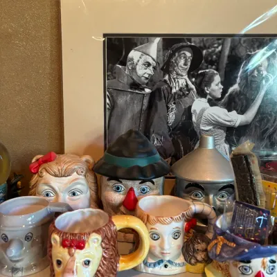 Collection of Wizard of Oz ceramic character mugs and cookie jars displayed in front of a matted black-and-white promotional photo.