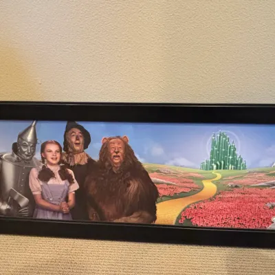 Framed panoramic print featuring main characters from 'The Wizard of Oz' along the Yellow Brick Road toward the Emerald City.