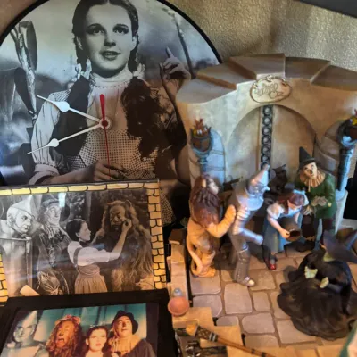 Collection of Wizard of Oz memorabilia, including a vinyl record clock featuring Dorothy, framed film photos, and a detailed character...