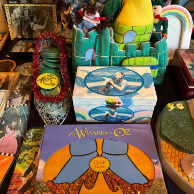 Sale Photo Thumbnail #128: Collection of The Wizard of Oz memorabilia, including a boxed Ruby Slippers mousepad, a printed jewelry box, plush Emerald City playset, and decorative figures.