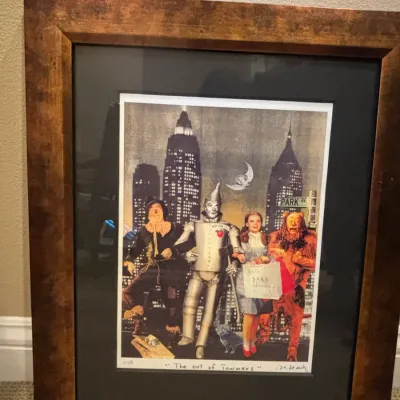 Framed pop art print titled "The Out of Towners," featuring Wizard of Oz characters in a New York City cityscape, presented in...