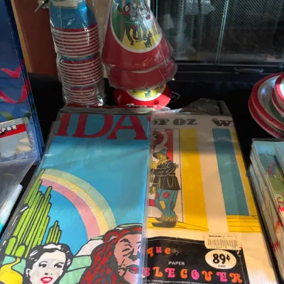 Sale Photo Thumbnail #113: Vintage Wizard of Oz themed birthday party supplies, including unopened paper table covers, cone party hats, paper cups, and napkins in original packaging.