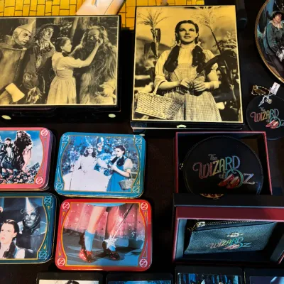 Sale Photo Thumbnail #123: Collection of Wizard of Oz memorabilia, including Coach leather goods in original boxes, decorative tins, framed black-and-white photos, and small themed collectibles.