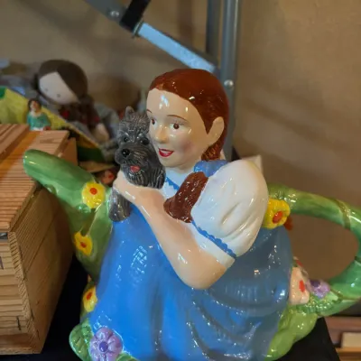 Vintage Wizard of Oz Dorothy and Toto glazed ceramic teapot in glossy finish, featuring floral accents and a leafy vine handle.