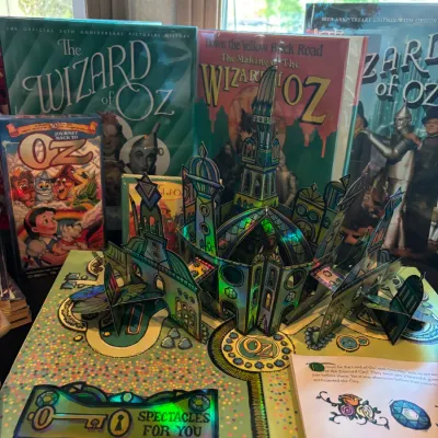 Collection of Wizard of Oz memorabilia, featuring a detailed pop-up book displaying the Emerald City, hardbound commemorative pictorial...